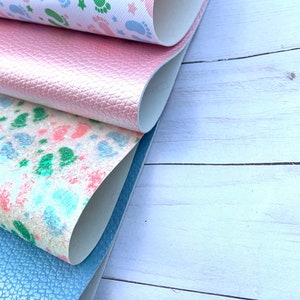 May include: Four different fabric swatches, one with a pink glitter finish, one with a blue glitter finish, one with a white background and green and blue footprints, and one with a white background and a watercolour-like design of green and pink footprints.