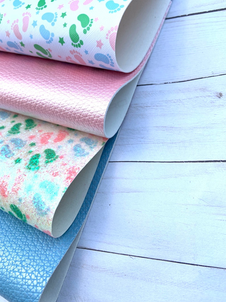 May include: Four different fabric swatches, one with a pink glitter finish, one with a blue glitter finish, one with a white background and green and blue footprints, and one with a white background and a watercolour-like design of green and pink footprints.