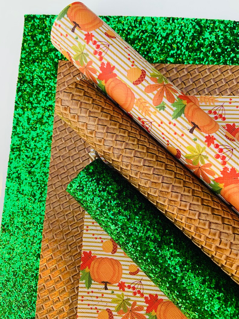 May include: An assortment of decorative craft materials, including rolls of patterned fabric and glitter sheets. The fabrics feature autumn-themed designs with pumpkins, leaves, and berries. The color palette includes green, brown, orange, and white.