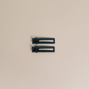 May include: Two black rectangular hair clips with a matte finish.