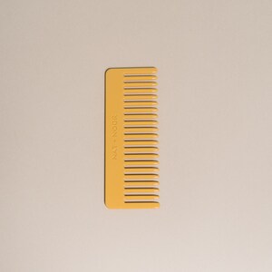 May include: A yellow plastic comb with the text "NAT + NOIR" printed on the side.