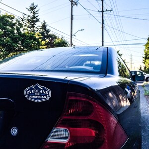 May include: A black Honda Civic EX with a "Overland The Americas" sticker on the back. The car has a red taillight and a silver trim around the taillight.