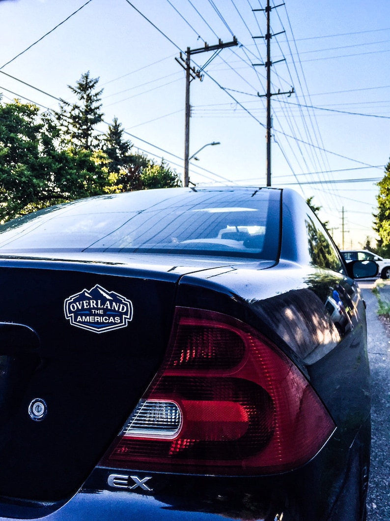 May include: A black Honda Civic EX with a "Overland The Americas" sticker on the back. The car has a red taillight and a silver trim around the taillight.