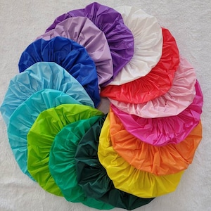 May include: A collection of colorful shower caps in various shades, including blue, green, yellow, orange, pink, red, purple, and white. The caps are arranged in a circular pattern, showcasing their vibrant colors and pleated design.