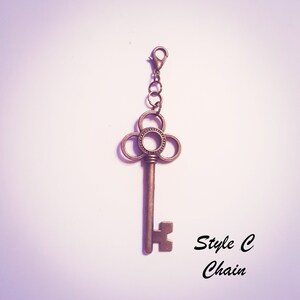 May include: A bronze-toned metal key charm featuring a decorative clover-shaped bow with a beaded center ring. The key is attached to a small jump ring and a lobster claw clasp. The text "Style C Chain" is printed in black in the lower right corner.