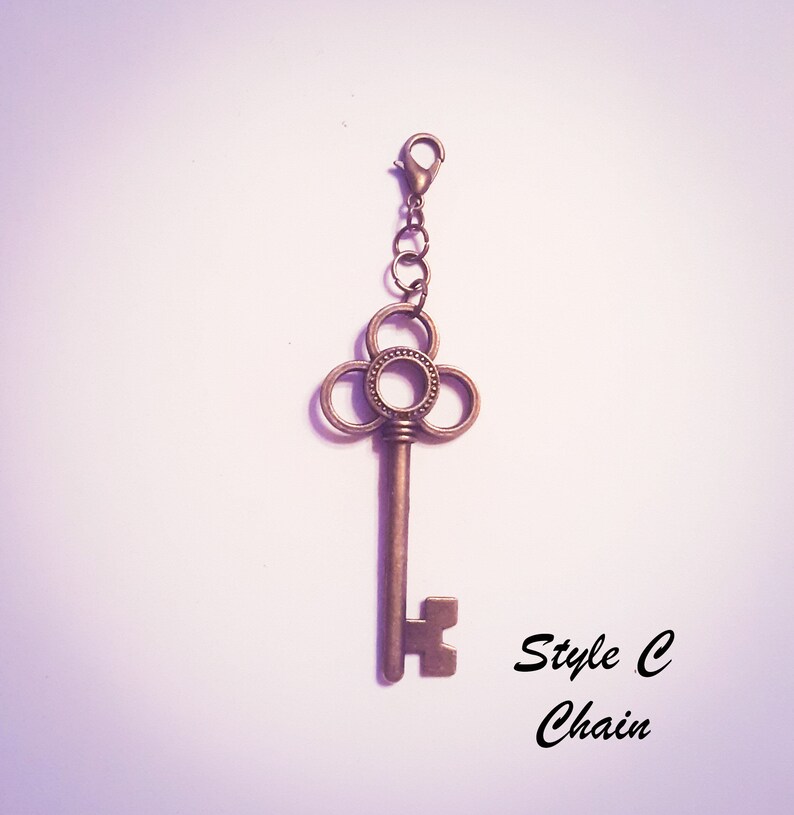 May include: A bronze-toned metal key charm featuring a decorative clover-shaped bow with a beaded center ring. The key is attached to a small jump ring and a lobster claw clasp. The text "Style C Chain" is printed in black in the lower right corner.