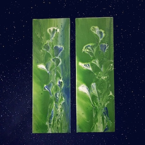 May include: Two green and blue abstract paintings with white floral designs. The paintings are on a dark blue background with white specks.