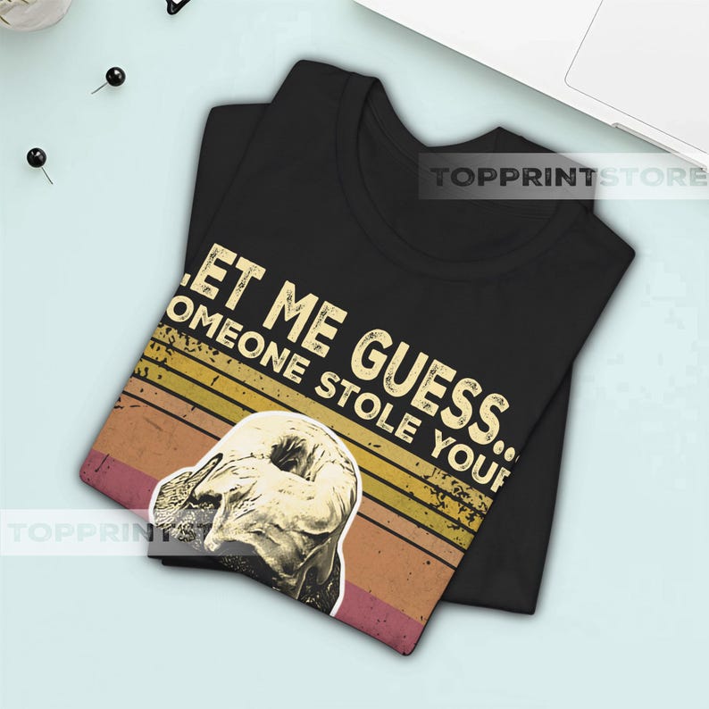 May include: Black t-shirt with the text "LET ME GUESS... SOMEONE STOLE YOUR..." in white. The shirt features a vintage-style graphic of a donut with a retro sunset design.