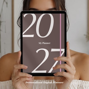 Könnte beinhalten: Ein digitales Tablet mit einem braunen Bildschirm, auf dem der große weiße Text 2027 und die zentrierten Wörter My Planner zu sehen sind. Eine dünne vertikale rosa Linie verläuft auf der rechten Seite. Der Text Personalized Digital Planner steht darunter.