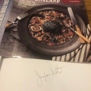 May include: A signed copy of the cookbook "Jasper White's Cooking from New England" with a photo of a dish on the cover. The book features over 300 traditional and contemporary recipes.