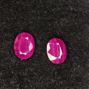 Op de afbeelding: Twee ovale, gefacetteerde robijn edelstenen met een diepe roze tint. De edelstenen zijn geplaatst tegen een zwarte fluwelen achtergrond.