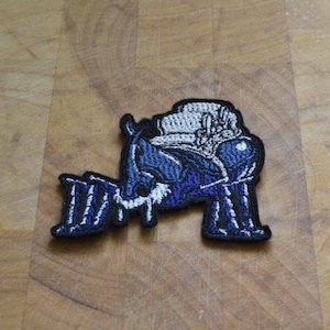 May include: Blue and white embroidered iron-on patch of a cartoon bug wearing a hat.