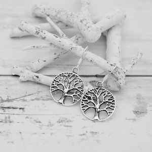 May include: A pair of silver earrings with a tree of life design. The earrings are hanging from a white background.