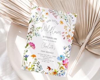 May include: A white invitation card with a floral border. The text reads "Our Little Wildflower is turning one. Join us to celebrate Charlotte's First Birthday. Saturday May 1st at 1:00 pm at Daisy Hill Drive, Rockville. RSVP to Sarah at 410-555-1212 by May 1st."