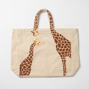 May include: A beige canvas tote bag featuring a giraffe family design. The bag has brown giraffe patterns on the front, with matching handles. The giraffe family includes a tall adult giraffe and two smaller giraffes.