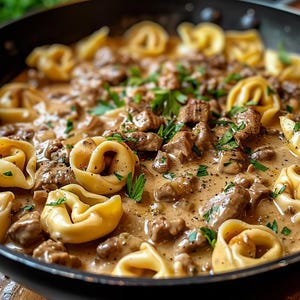 Könnte beinhalten: Nahaufnahme einer Bratpfanne gefüllt mit cremiger Pilz- und Rindfleischsauce mit frischer Petersilie und gekochten Nudeln. Die Nudeln sind ringförmig mit einem Loch in der Mitte.