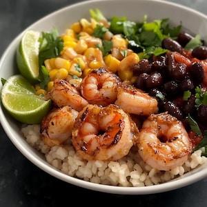 Può includere: Una ciotola bianca piena di un pasto colorato e delizioso. La ciotola contiene riso bianco, mais, fagioli neri, coriandolo, spicchi di lime e gamberi.