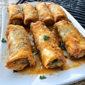 Peut inclure: Une assiette blanche présente plusieurs rouleaux aux œufs croustillants et dorés. Les rouleaux sont recouverts d'une panure et une garniture verte est visible. Une sauce claire et du persil garnissent l'assiette.