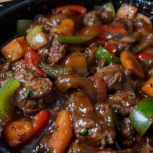 Puede incluir: Primer plano de un plato sabroso con trozos de carne, pimientos rojos, verdes y amarillos vibrantes y rodajas de zanahoria. Los ingredientes están cubiertos con una salsa rica y brillante. El texto "TEES EATS & THINGS" es visible en el fondo.