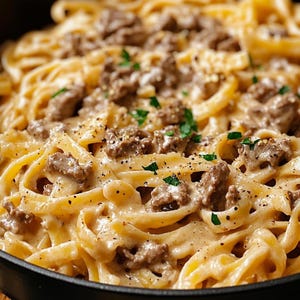 Puede incluir: Primer plano de un bol de pasta cremosa con carne picada y hierbas. La pasta está cocinada al dente y la salsa es rica y sabrosa.