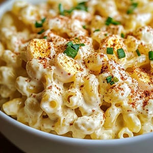 Può includere: Un primo piano di una ciotola di insalata di maccheroni con un condimento cremoso, cipolle verdi tritate e una spolverata di paprika.