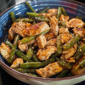 Può includere: Primo piano di una ciotola piena di un piatto di pollo e fagiolini. Il pollo dorato è tagliato a pezzi. I fagiolini sono verdi e mescolati con il pollo. Un pasto sano e appetitoso.