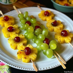 Puede incluir: Un plato blanco con una variedad de brochetas de fruta. Las brochetas están hechas con piña, cerezas y uvas verdes. Las brochetas están dispuestas en un patrón decorativo en el plato. El plato está sobre una mesa de madera.