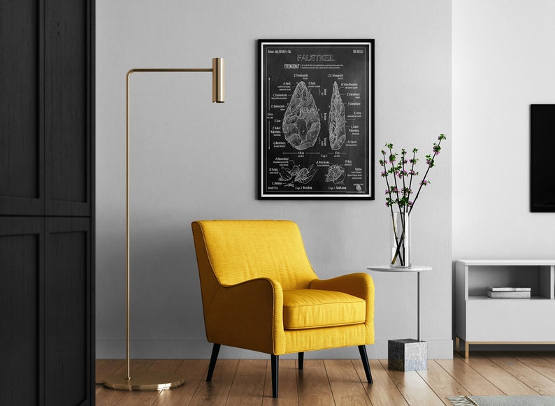 Pode incluir: Uma ilustra&ccedil;&atilde;o em preto e branco de um machado de m&atilde;o, ou 'Faustkeil', sobre um fundo de quadro-negro. A ilustra&ccedil;&atilde;o &eacute; emoldurada e pendurada em uma parede branca acima de uma poltrona amarela.