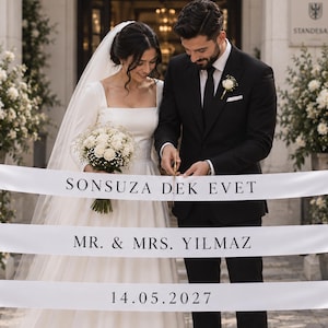 Könnte beinhalten: Ein langes weißes Satinband mit schwarzem Aufdruck, der SONSUZA DEK EVET, MR. & MRS. YILMAZ und 14.05.2027 lautet. Das Band wird horizontal gehalten und zeichnet sich durch eine glatte Textur sowie eine klare, schlichte Typografie aus.