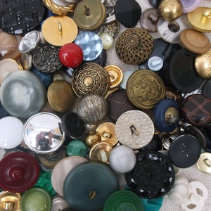 May include: A selection of vintage buttons in various sizes, shapes, and colours. The buttons include gold, silver, black, red, green, and blue. Some buttons have intricate designs, while others are plain.