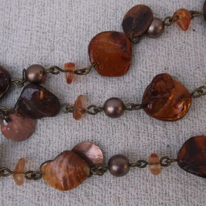 Puede incluir: Un collar marrón y dorado con cuentas redondas y ovaladas. Las cuentas están hechas de diferentes materiales, incluyendo metal, vidrio y madera.