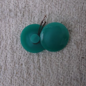 May include: Two teal green round buttons with a brown string connecting them.