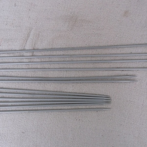 Puede incluir: Un juego de 10 agujas de tejer plateadas, con tamaños que van del 0 al 9. Las agujas están dispuestas en una fila, con la aguja más pequeña a la izquierda y la aguja más grande a la derecha.