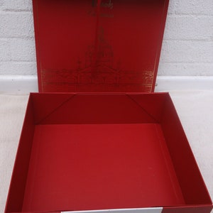 Puede incluir: Una caja de regalo roja vacía con una cinta blanca y las palabras "Harrods" en letras doradas en la tapa. La caja está abierta y el interior está forrado con papel rojo.