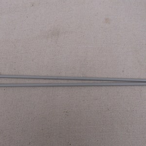 Puede incluir: Un par de agujas de tejer grises con una etiqueta de tamaño 5 1/2 en un extremo.