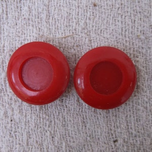 May include: Two red plastic buttons with a smaller red circle in the center of each button.