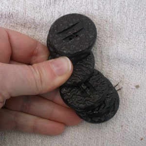 May include: A stack of four black buttons with a textured surface. The buttons have two holes each.
