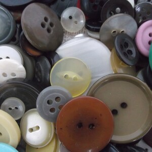 May include: A collection of assorted buttons in a variety of colours, shapes and sizes. The buttons are made from plastic, metal and wood. Some of the buttons have two holes, while others have four holes. The buttons are arranged in a random pattern.