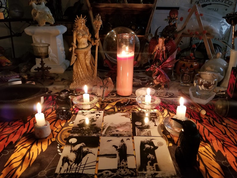 以下が含まれることがあります： ろうそく、女性の像、クリスタルボール、タロットカードなど、さまざまな物が置かれた、暗くて神秘的な祭壇。祭壇は黒とオレンジの模様の布で覆われています。