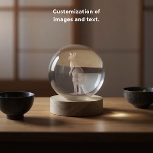 May include: A clear glass sphere featuring a 3D kangaroo design, set on a wooden base. The text "Customization of images and text" is visible. The sphere is displayed on a wooden table, with two dark bowls in the background.