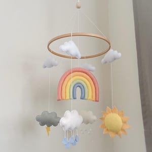 May include: A felt baby mobile with a rainbow, clouds, sun, and raindrops. The mobile is made of soft, colorful felt and is perfect for a nursery or child's room.
