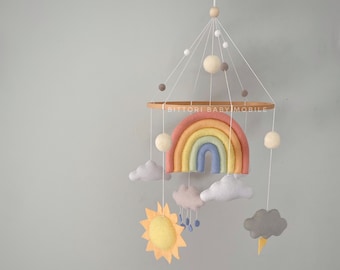 Rainbow nursery decor with sun, cloud with raindrops, cloud with lightning in pastel color palette. Weather baby mobile with felt balls