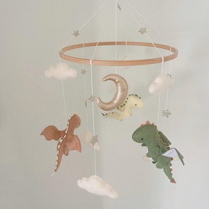 May include: A wooden baby mobile with a crescent moon, clouds, and three felt dragons. The dragons are green, brown, and yellow. The mobile is decorated with glitter stars.