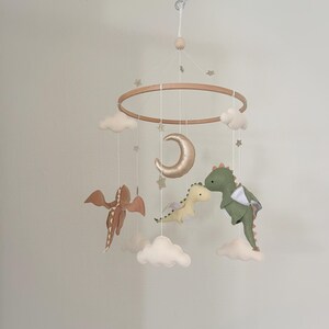 May include: A wooden baby mobile with a gold crescent moon, two felt dragons, and white clouds. The mobile is decorated with gold glitter stars.