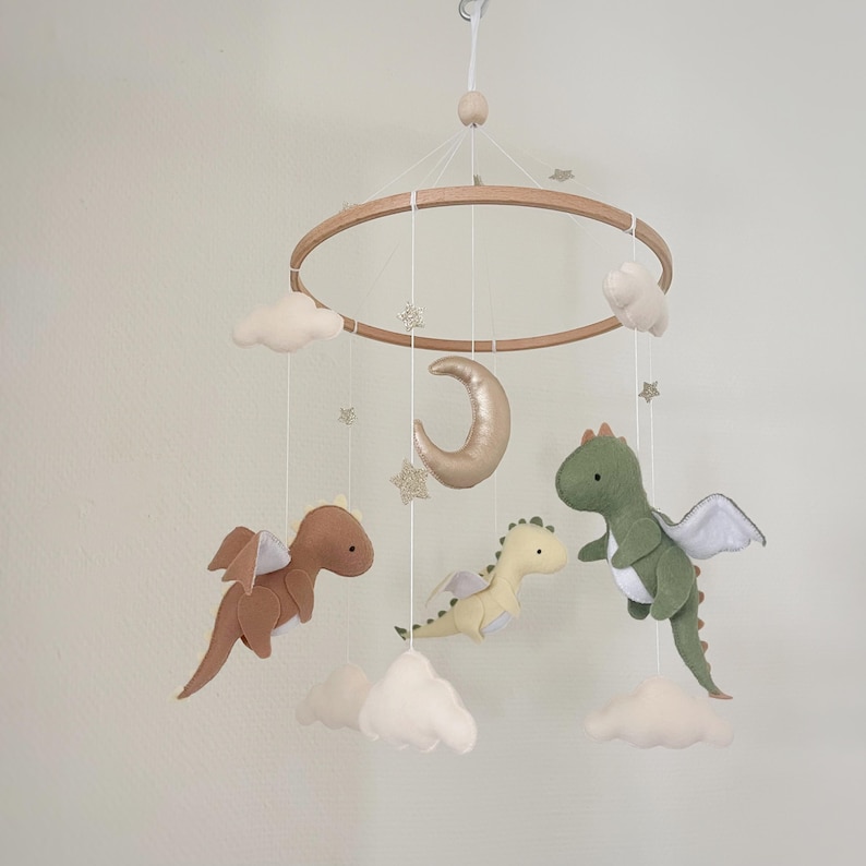 May include: A wooden baby mobile with a gold crescent moon, clouds, and three felt dragons in green, brown, and yellow.