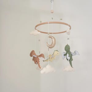 May include: A wooden baby mobile with a crescent moon, clouds, and three felt dragon toys. The dragons are green, brown, and cream.