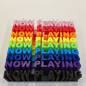 May include: A rainbow-colored stack of 3D printed blocks spelling "NOW PLAYING" in all caps.