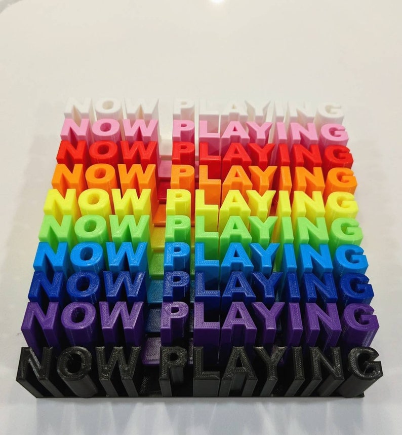 May include: A rainbow-colored stack of 3D printed blocks spelling "NOW PLAYING" in all caps.