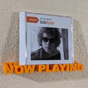 May include: A 3D printed orange plastic sign that says "NOW PLAYING" with a CD case behind it. The CD case has a black and white photo of Bob Dylan on the front with the text "playlist: the very best of bobdylan".