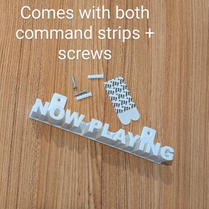 May include: White plastic sign that reads "NOW PLAYING" with screws and command strips for hanging.